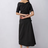 A woman modeling a black off-the-shoulder midi dress with short sleeves and a flared skirt, shown from the back against a light gray studio background.