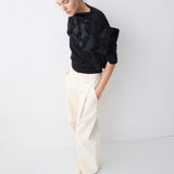 Person wearing a black sweater and white pants against a white background