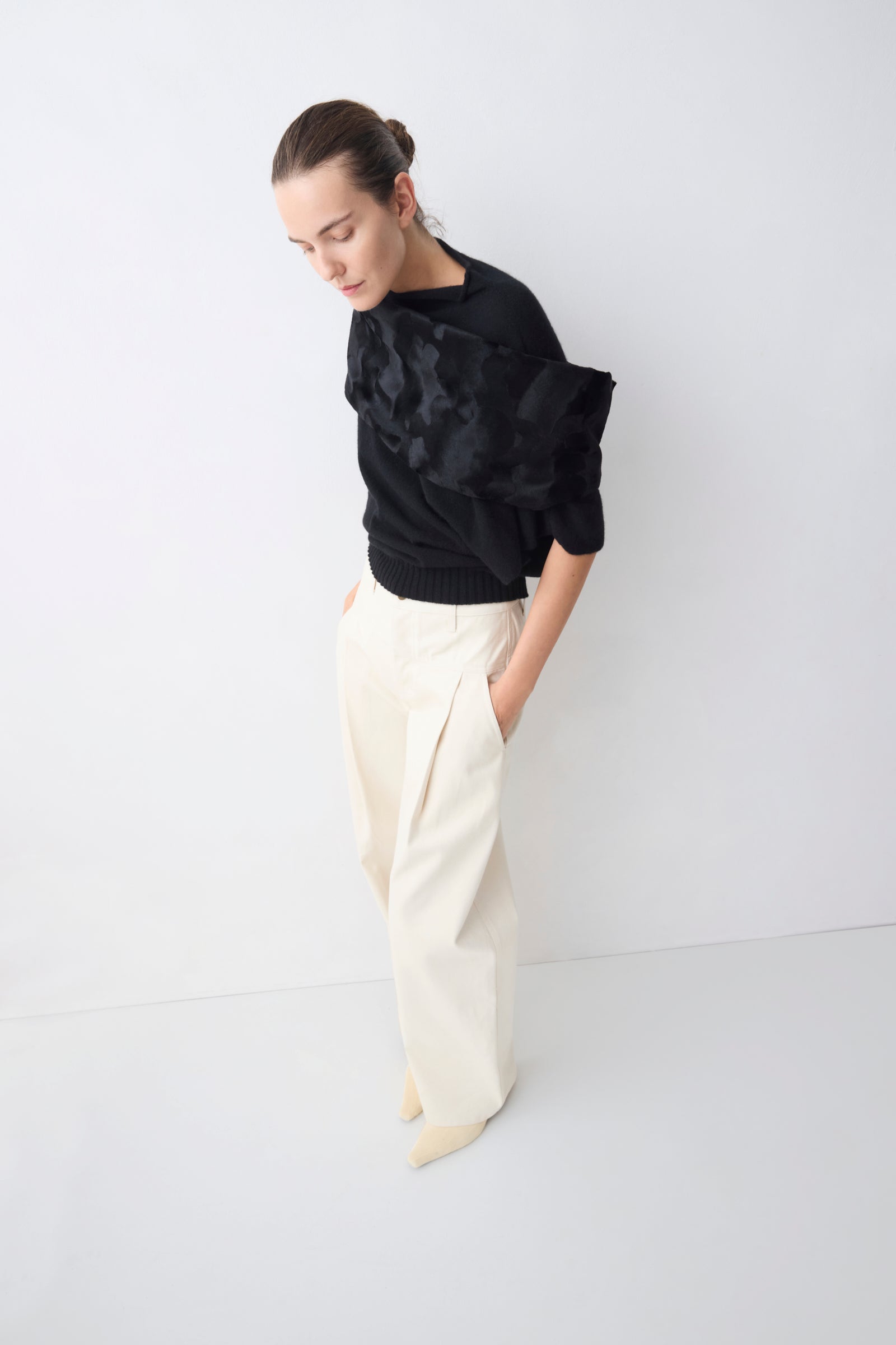 Person wearing a black sweater and white pants against a white background