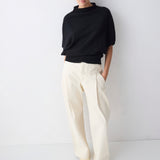 Person wearing a black sweater and white pants against a white background