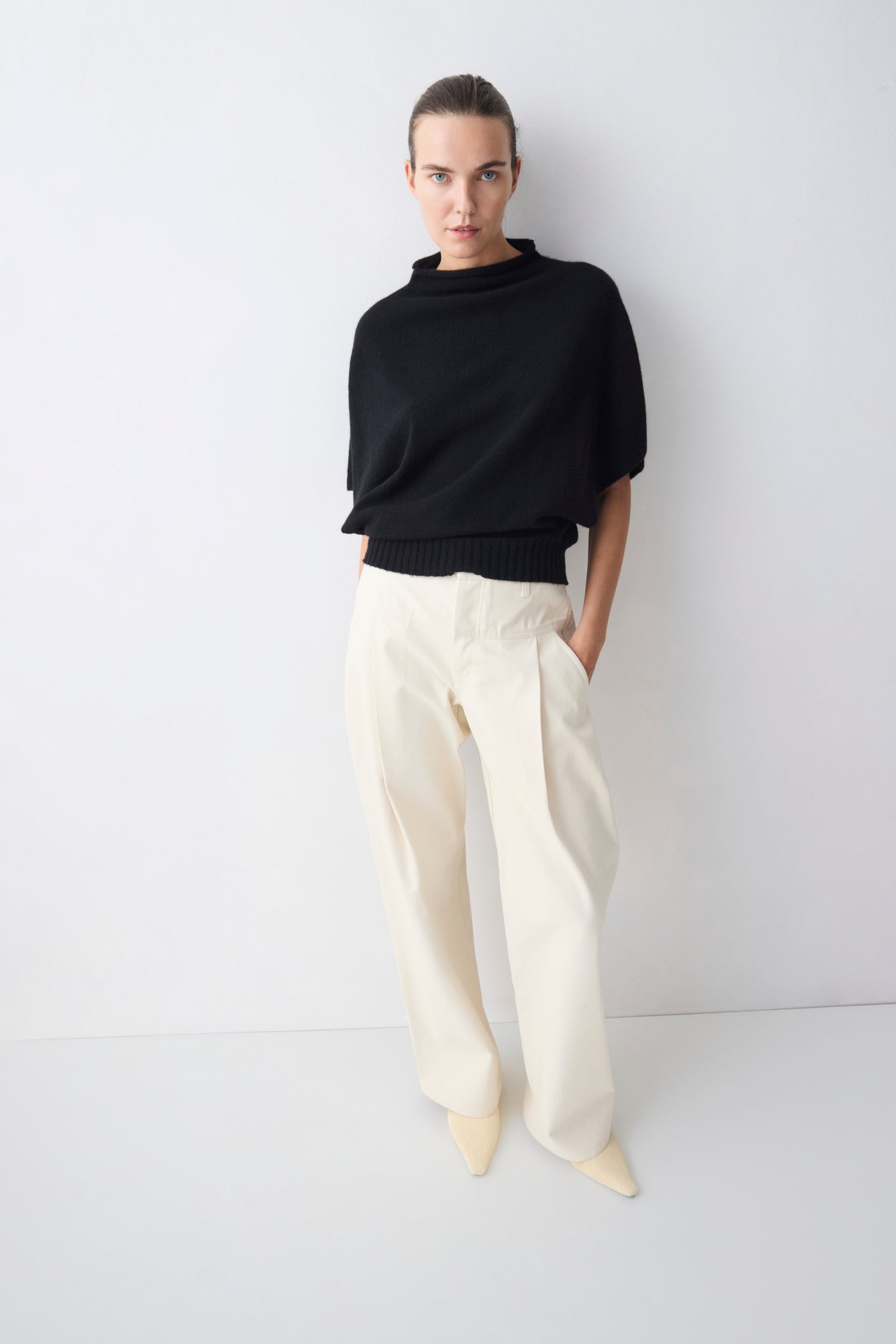Person wearing a black sweater and white pants against a white background