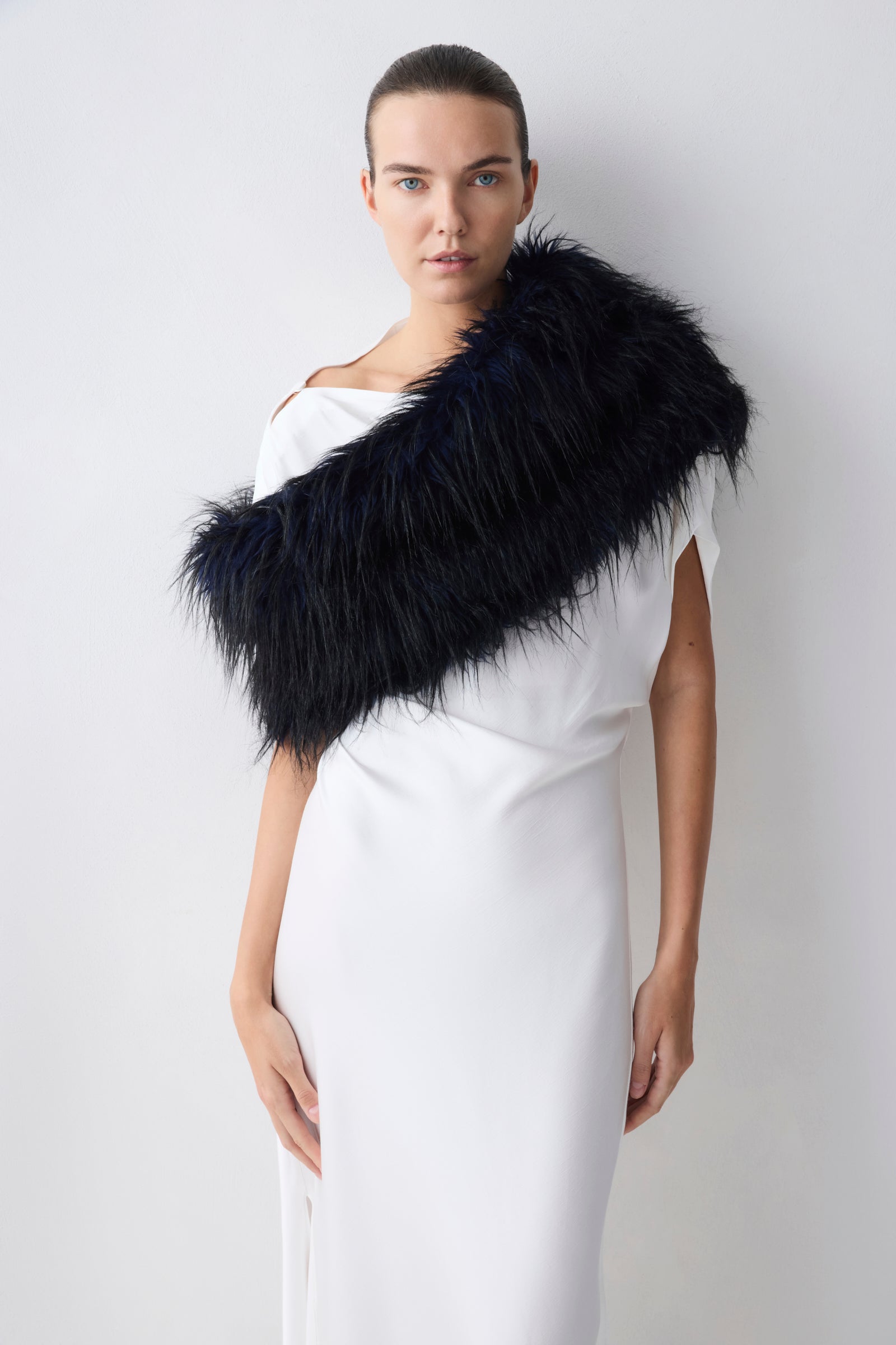 Woman wearing a navy fur shrug over a white dress against a plain background