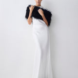 Woman wearing a navy fur shrug over a white dress on a plain background