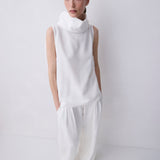 A model wearing a white sleeveless mock-neck top and matching wide-leg trousers, standing against a plain white studio background.