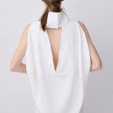 A model shown from the back wearing a white sleeveless top with a high structured collar and a deep V-back cutout, paired with matching white trousers, against a light gray studio background.