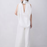 A model shown from the back wearing a white sleeveless jumpsuit with a high structured collar and a deep open back, paired with matching wide-leg trousers, set against a plain light gray studio background.
