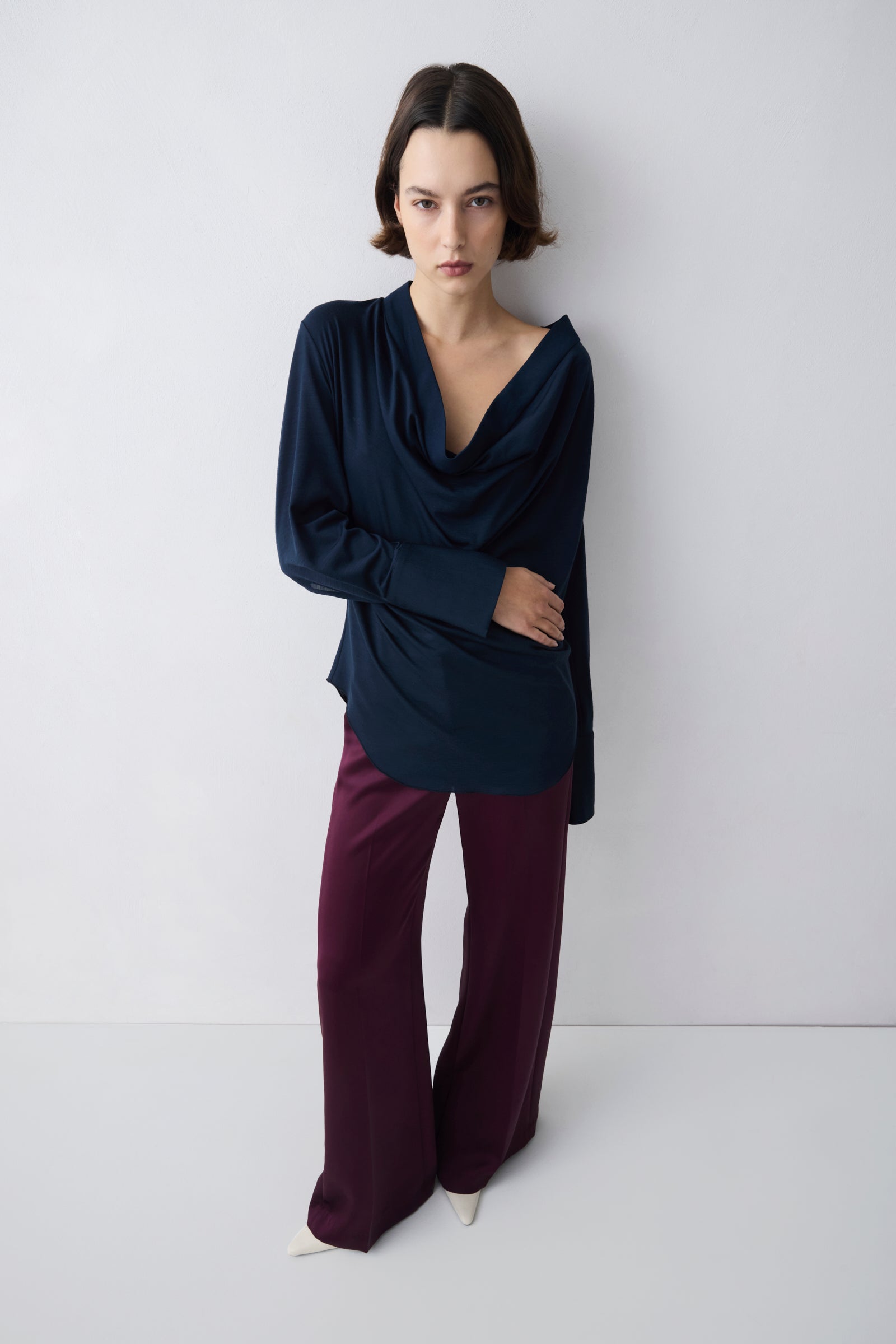 Woman wearing a dark blue top and purple pants against a white background