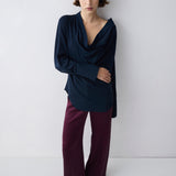 Woman wearing a dark blue top and purple pants against a white background