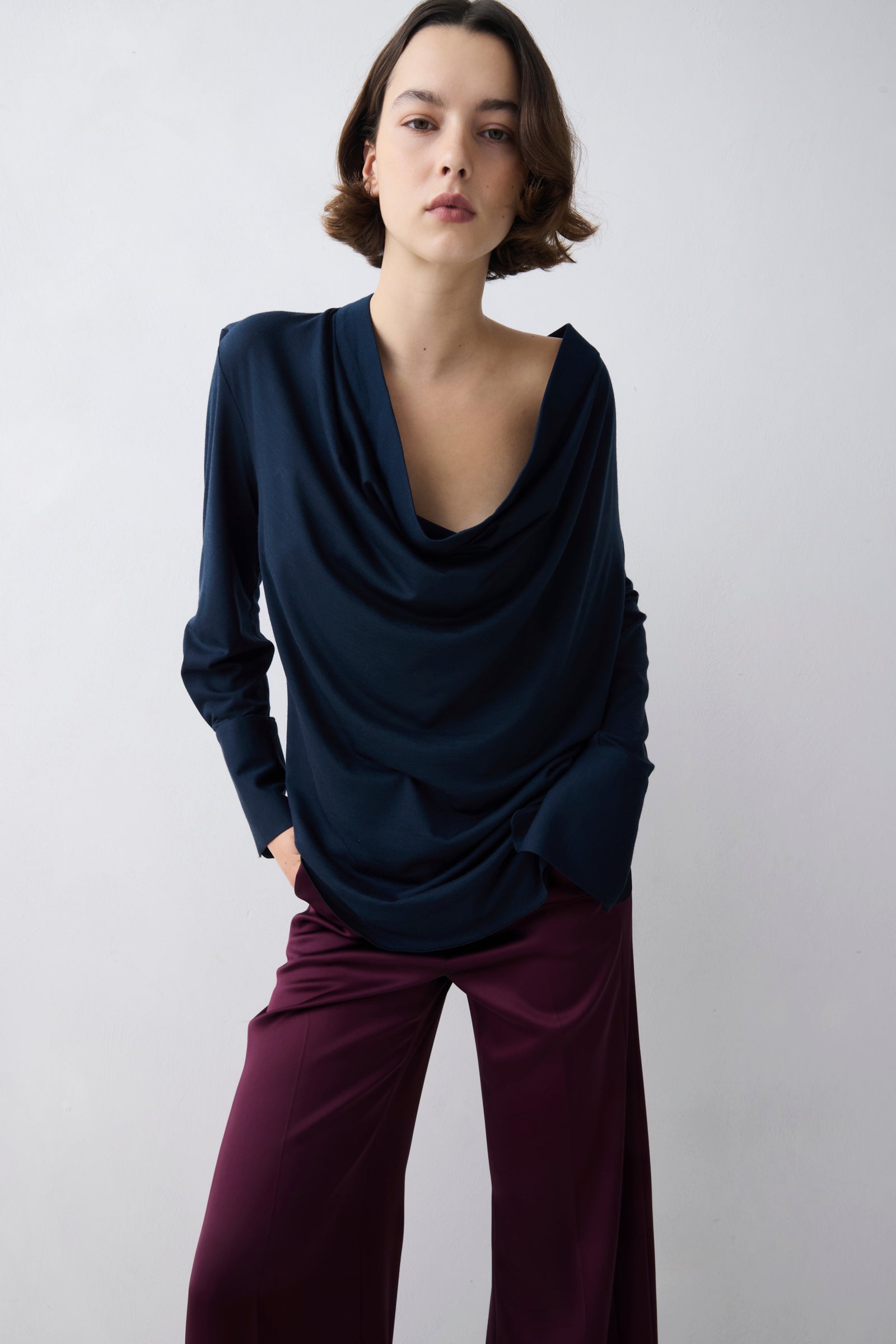 Woman wearing a navy blue top and purple pants against a white background