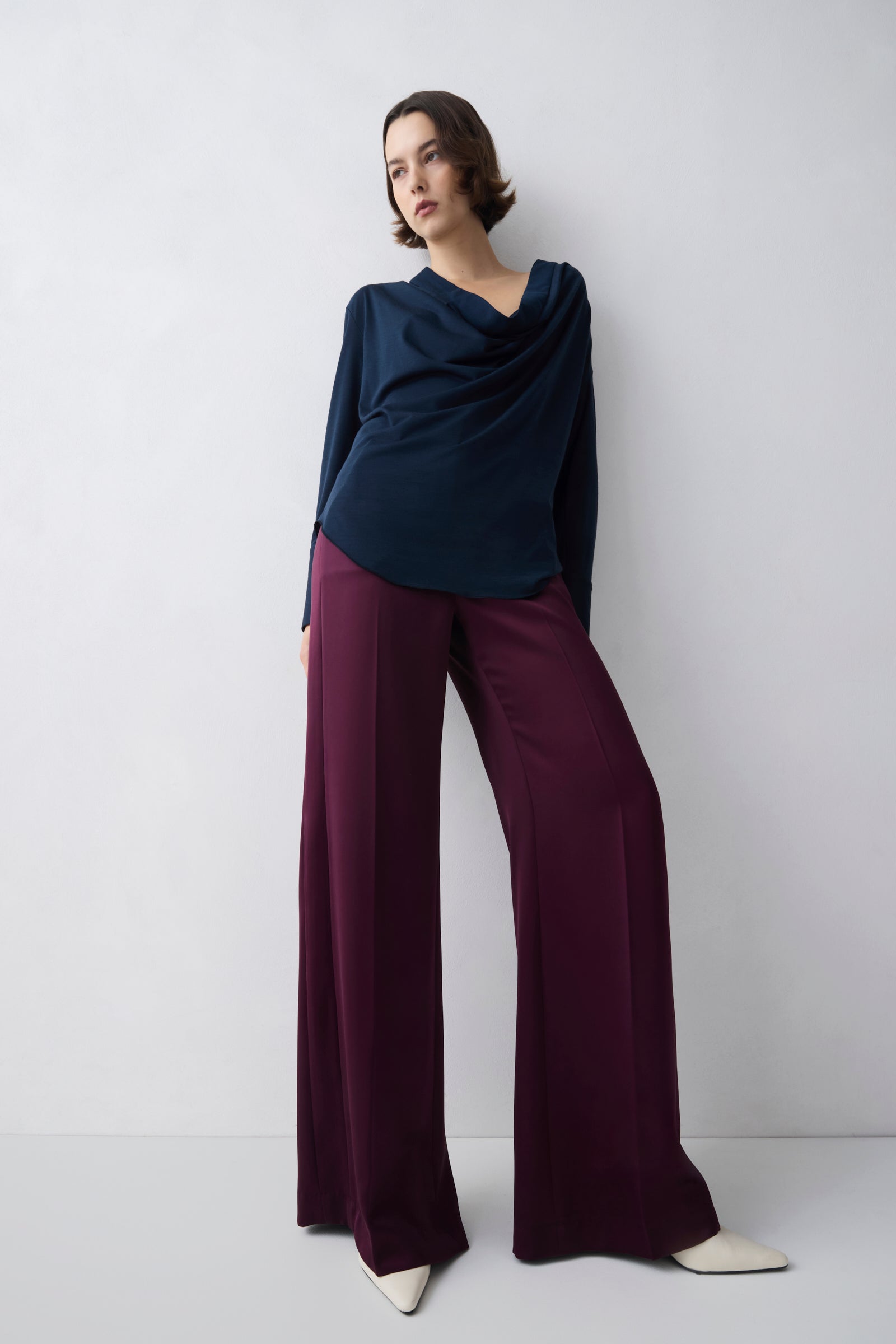 Woman wearing a navy top and maroon pants against a white background