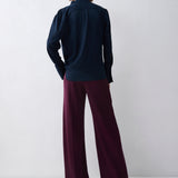 Person wearing a navy blazer and burgundy pants against a white background