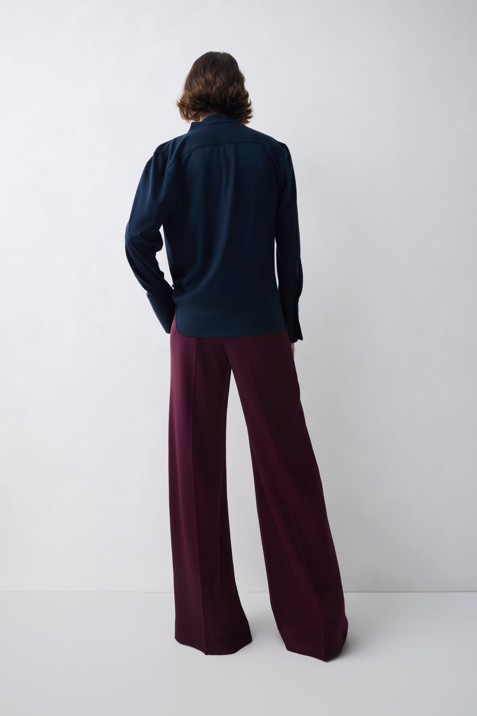 Person wearing a navy blazer and burgundy pants against a white background