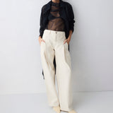 Person wearing a black sheer top, black cardigan, and white pants against a white background