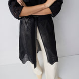 Person wearing a black textured dress with white shoes on a plain background