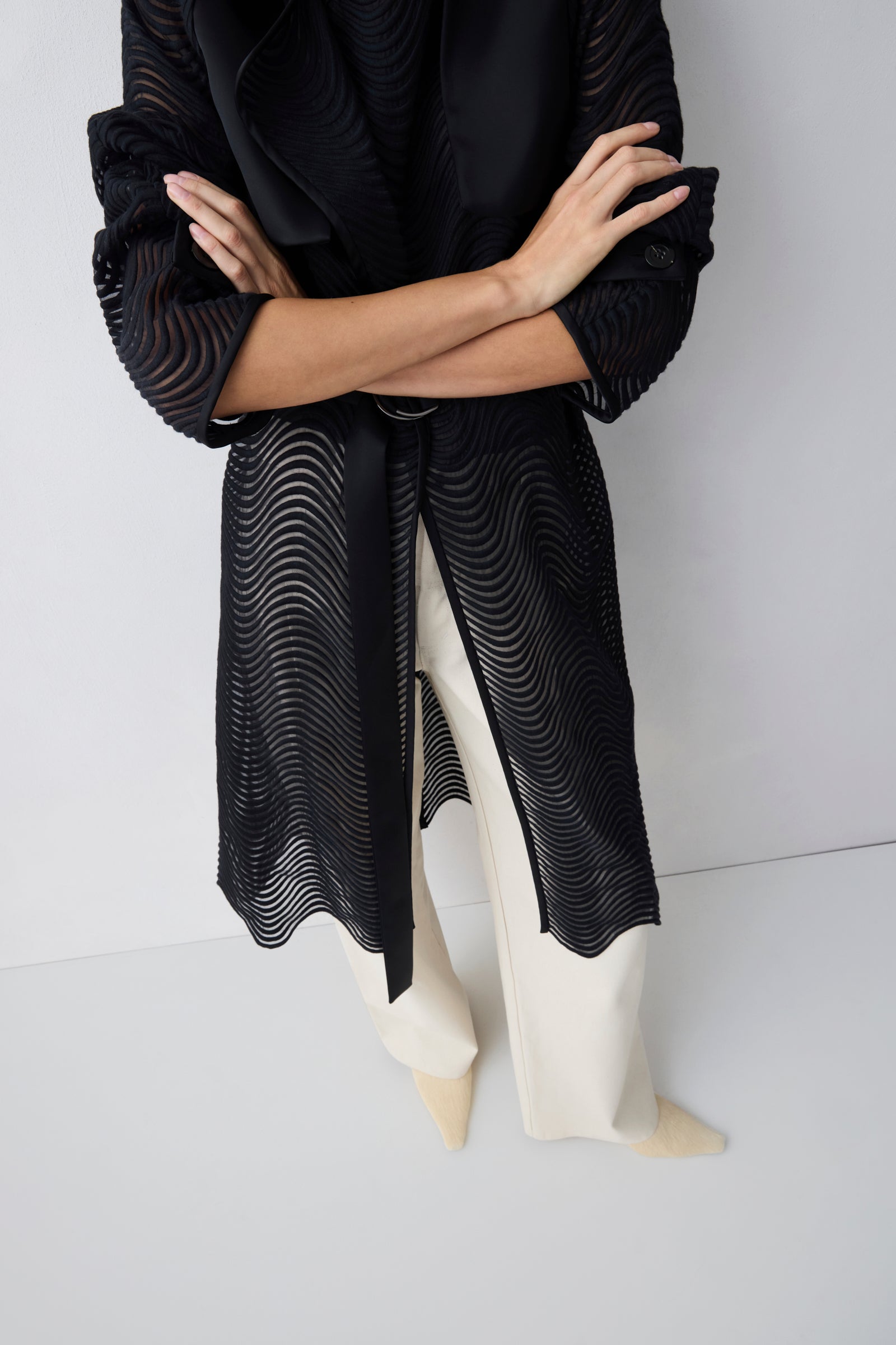 Person wearing a black textured dress with white shoes on a plain background