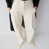 Person wearing white pants with a black top on a plain background