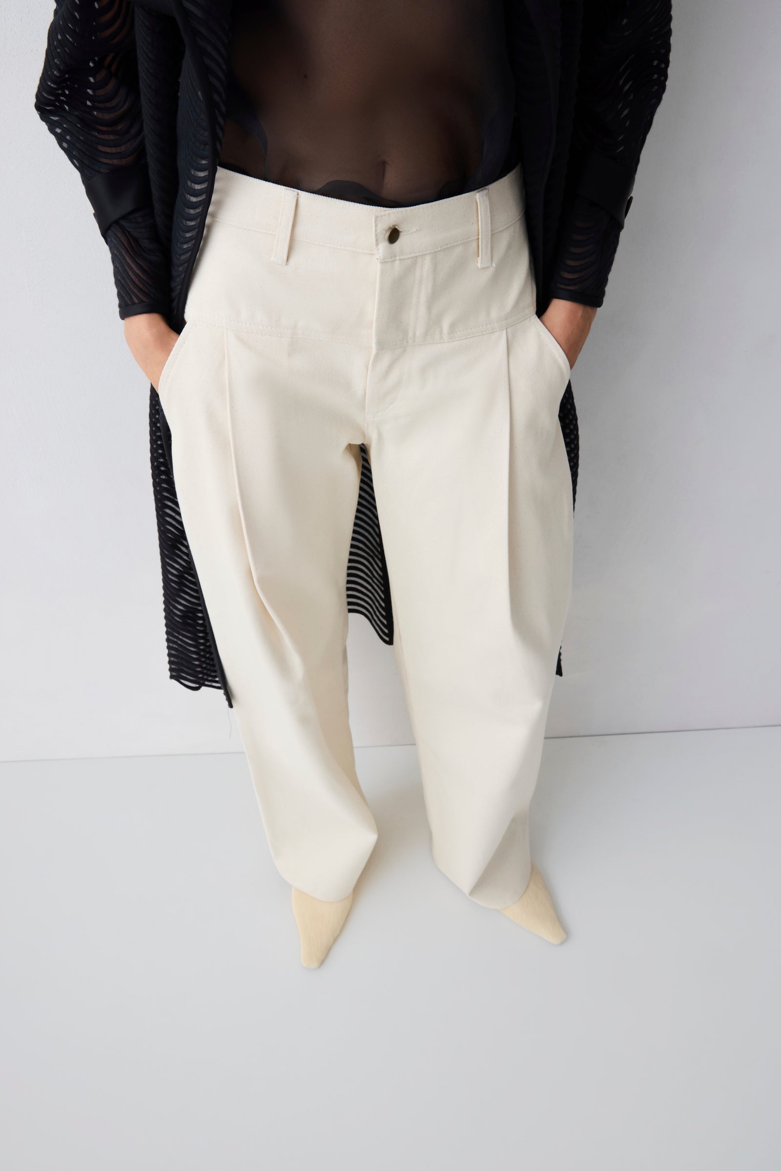 Person wearing white pants with a black top on a plain background