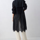 Person wearing a black coat over a patterned dress on a white background