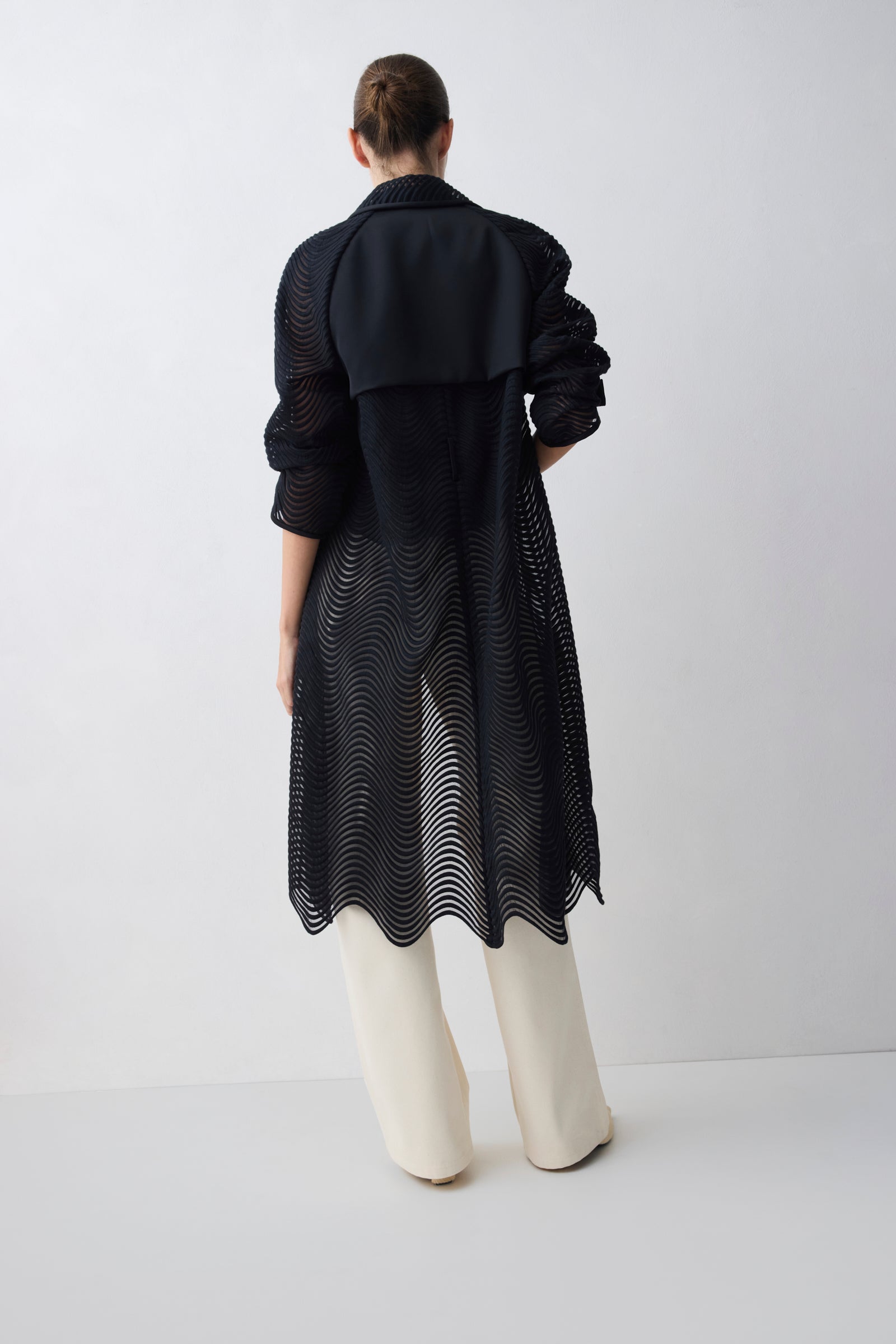 Person wearing a black coat over a patterned dress on a white background