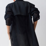 Person wearing a long black textured coat on a white background