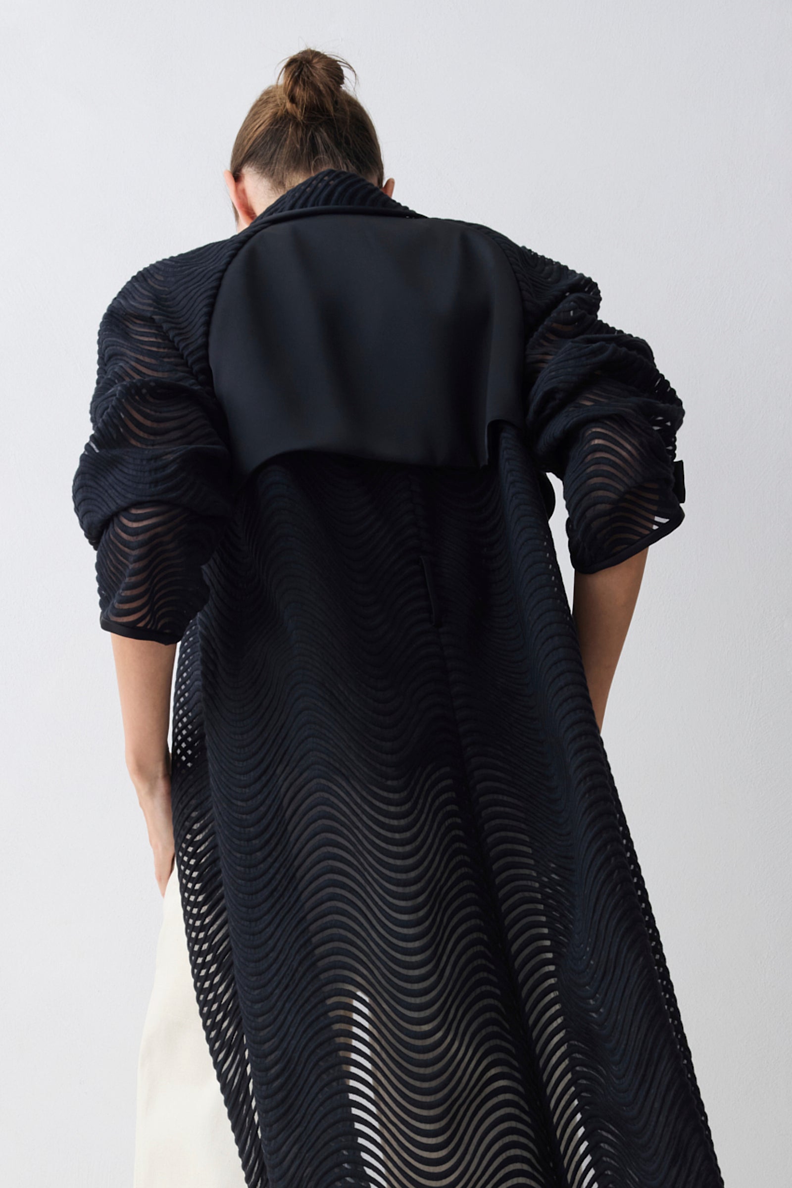 Person wearing a long black textured coat on a white background