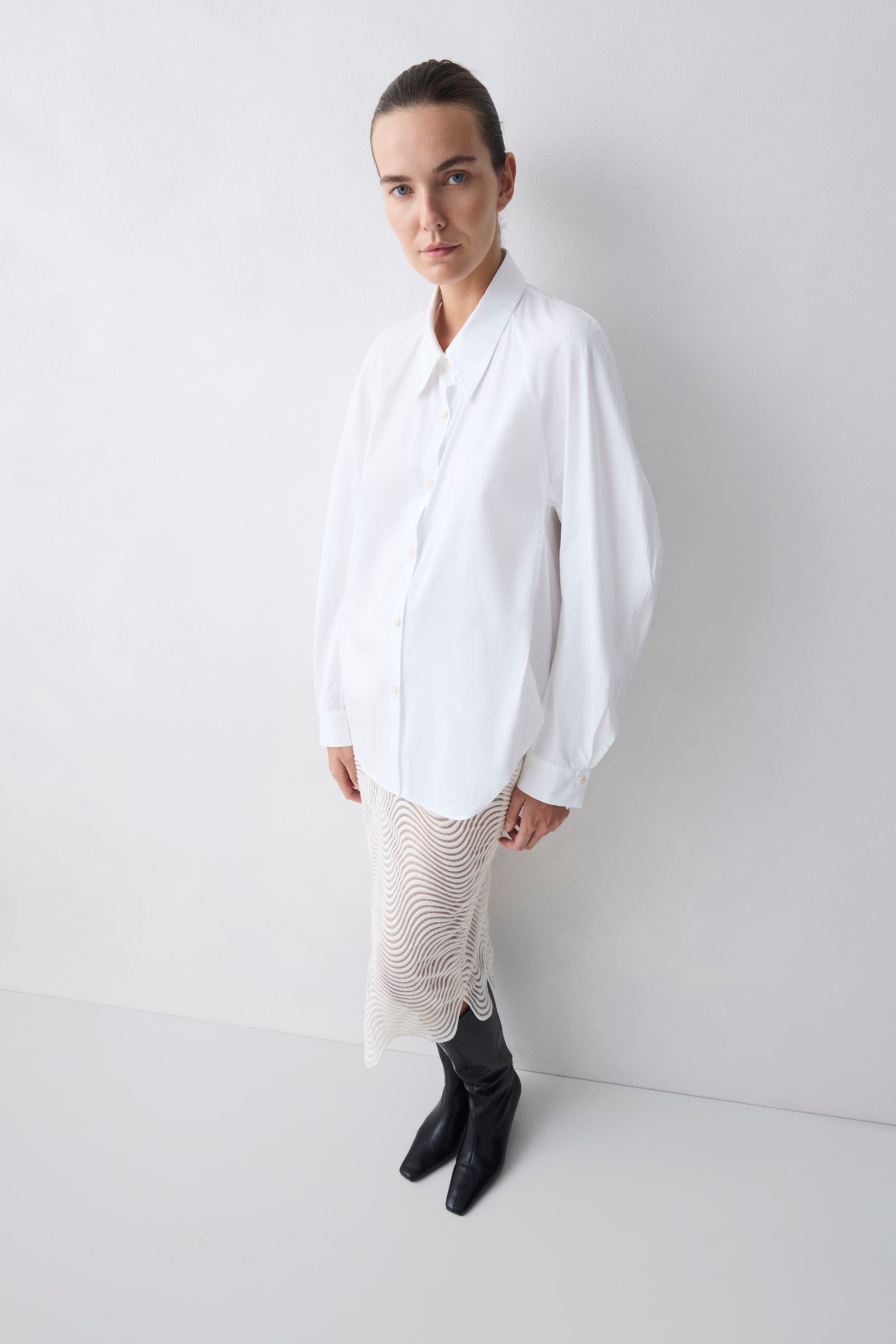 Person wearing a white shirt and black boots on a plain background