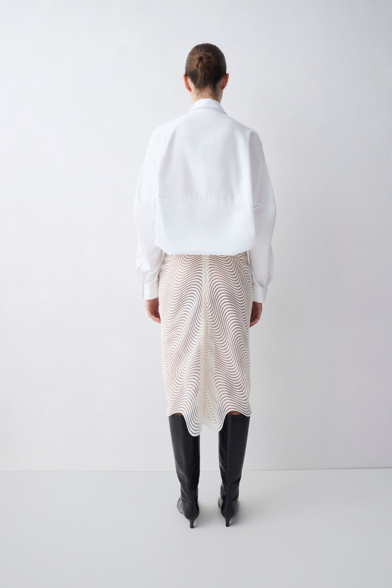 Person wearing a white shirt and patterned skirt with black boots on a white background