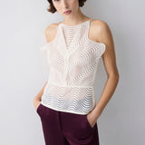 Woman wearing a white sleeveless top with a wavy pattern and purple pants against a light gray background