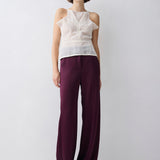 Woman wearing a white sleeveless top and purple pants against a white background