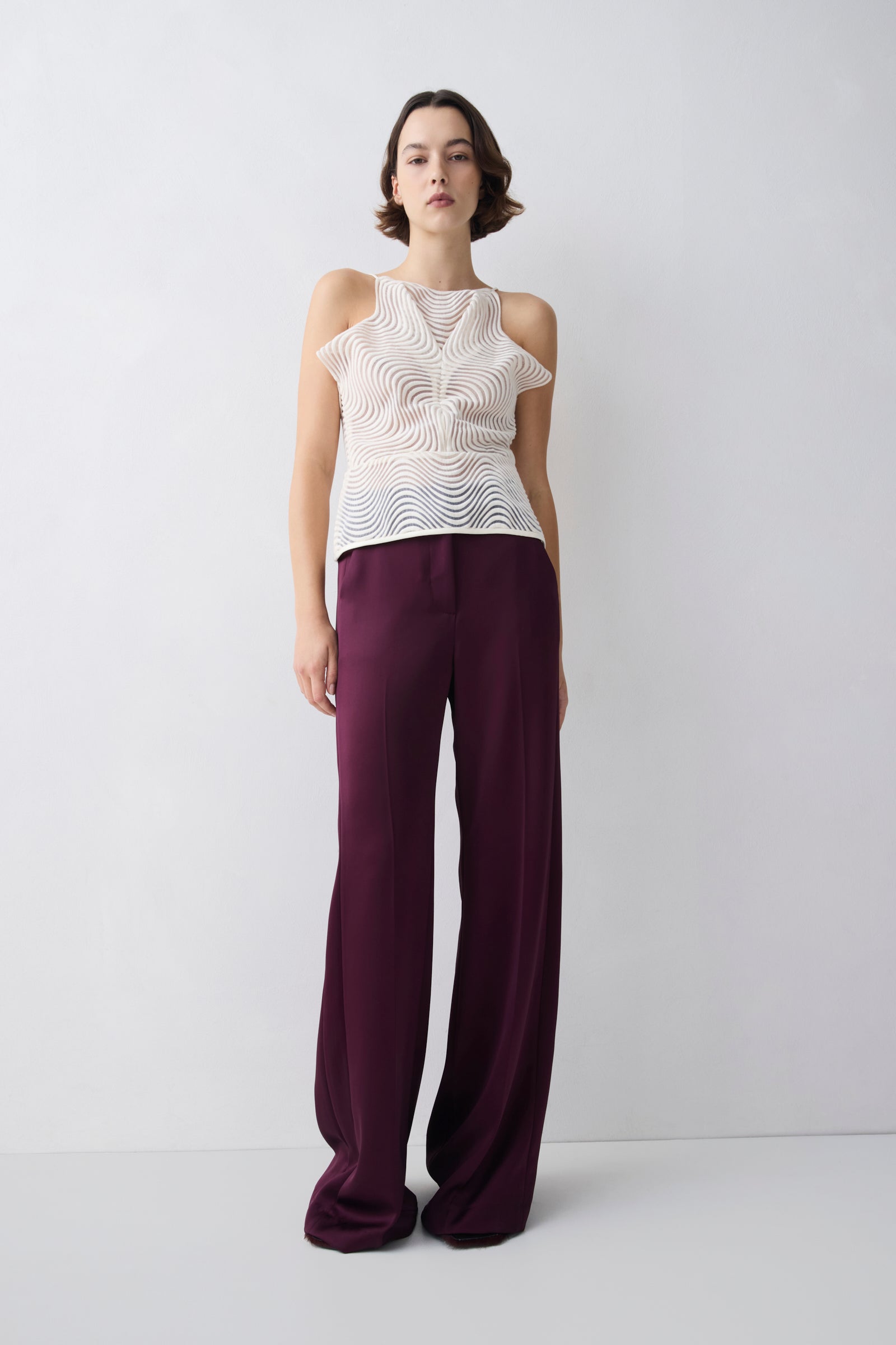 Woman wearing a white sleeveless top and purple pants against a white background