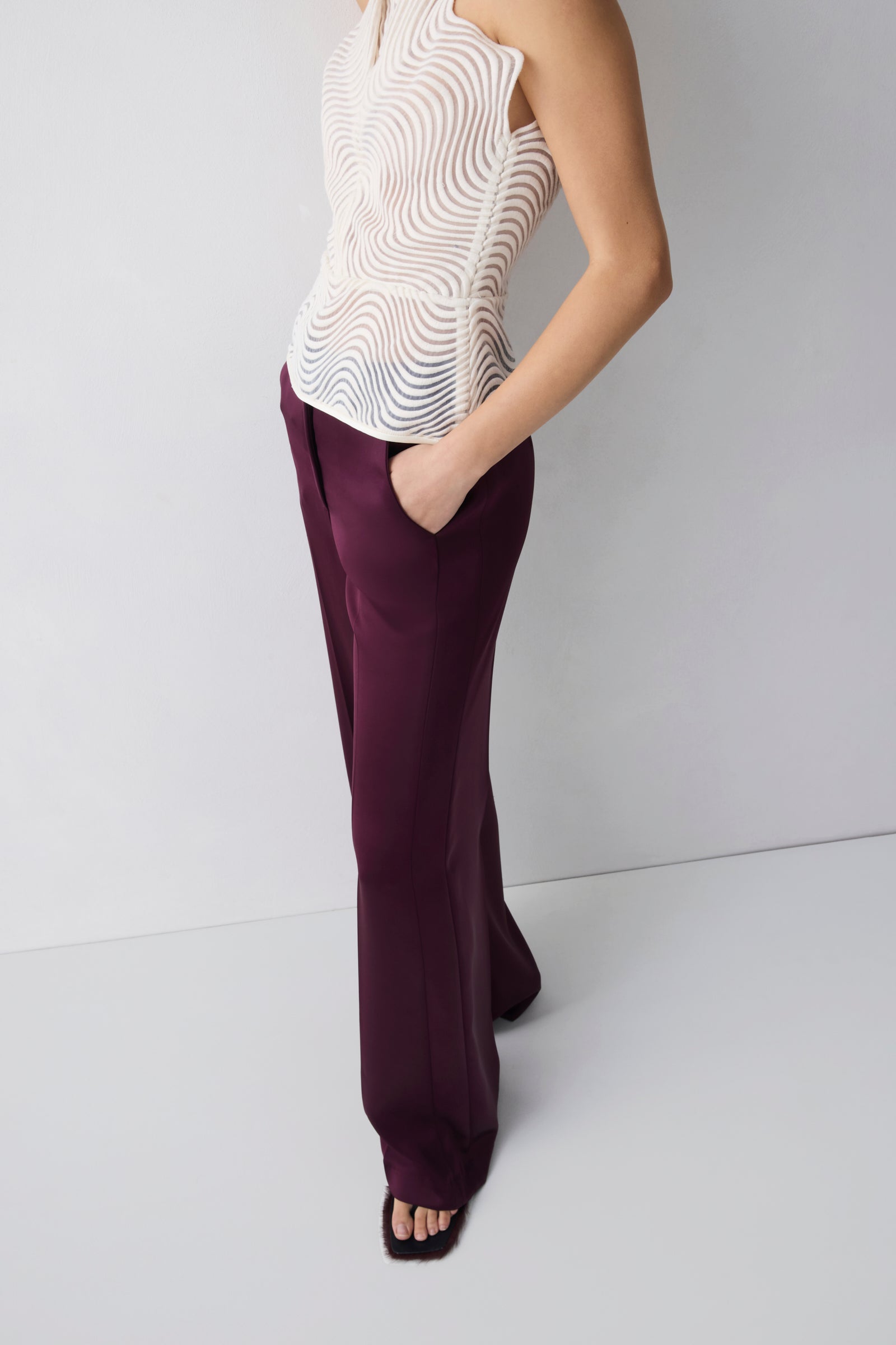 Person wearing a white patterned top and purple pants on a plain background