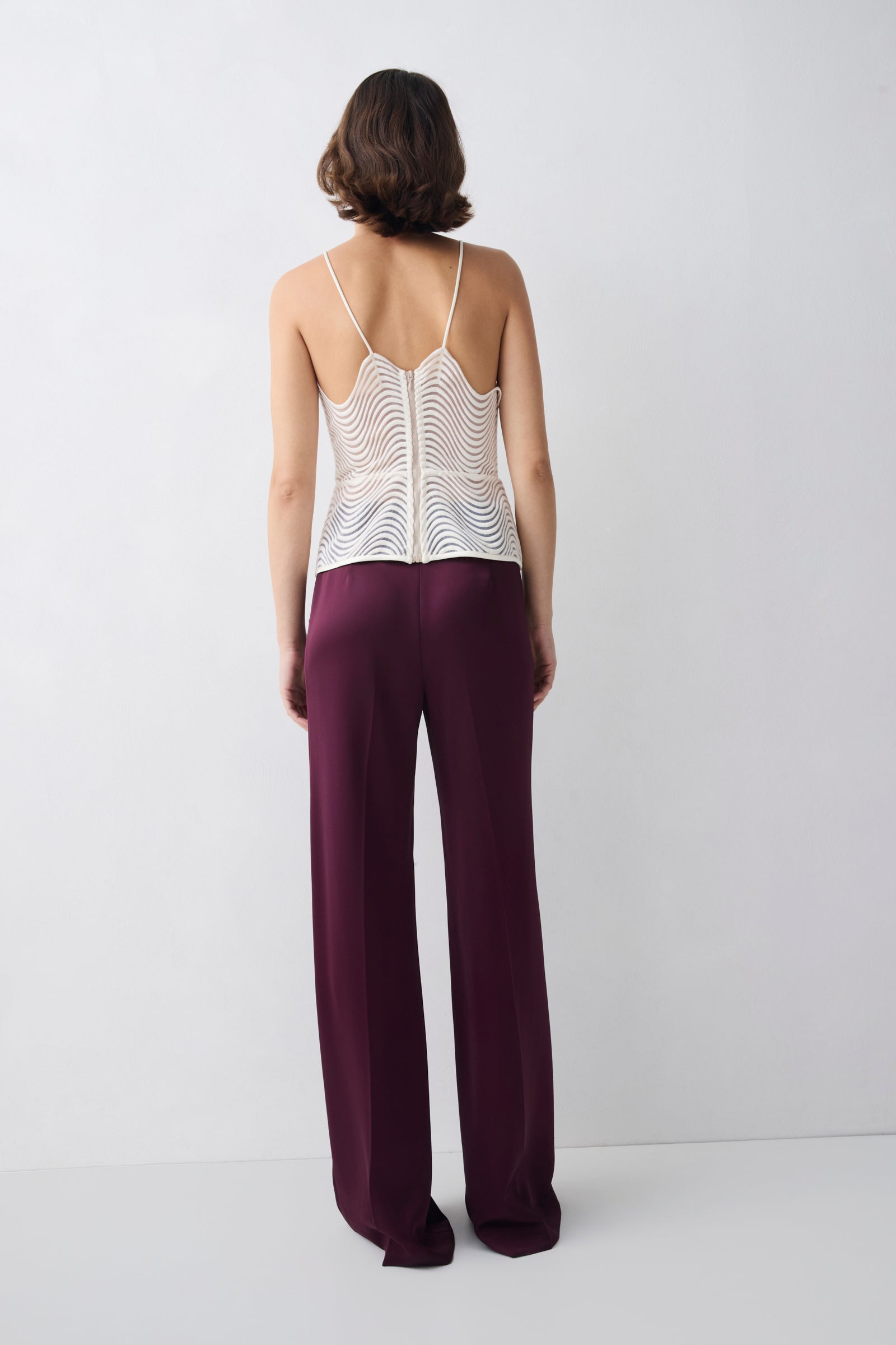 Woman wearing a white lace top and burgundy pants on a white background