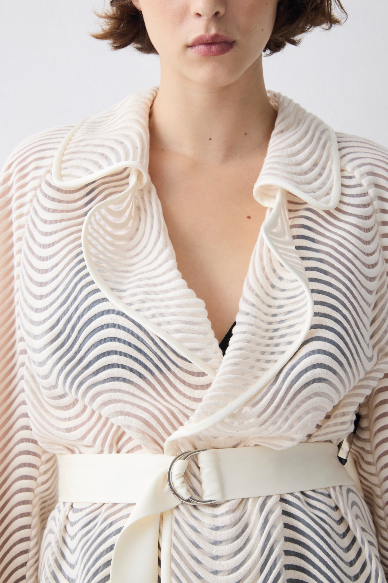 Person wearing a textured white garment with a belt against a plain background