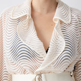 Person wearing a textured white garment with a belt against a plain background