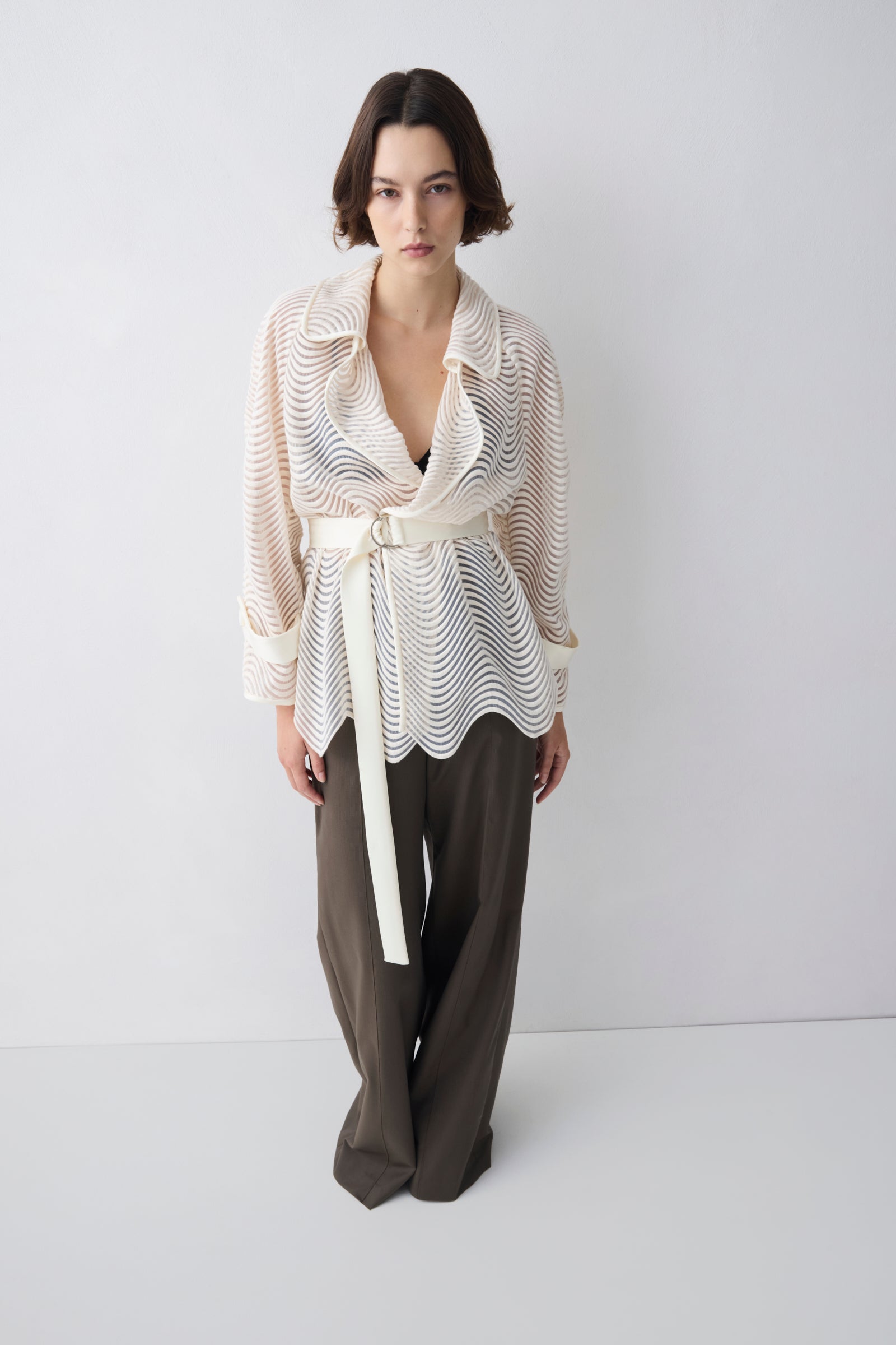 Woman wearing a white patterned top and brown pants on a white background