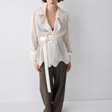 Woman wearing a white patterned top and brown pants on a white background