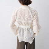 Person wearing a white patterned shirt and brown pants on a plain background