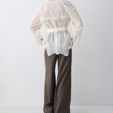 Person wearing a white patterned blouse and brown pants on a white background