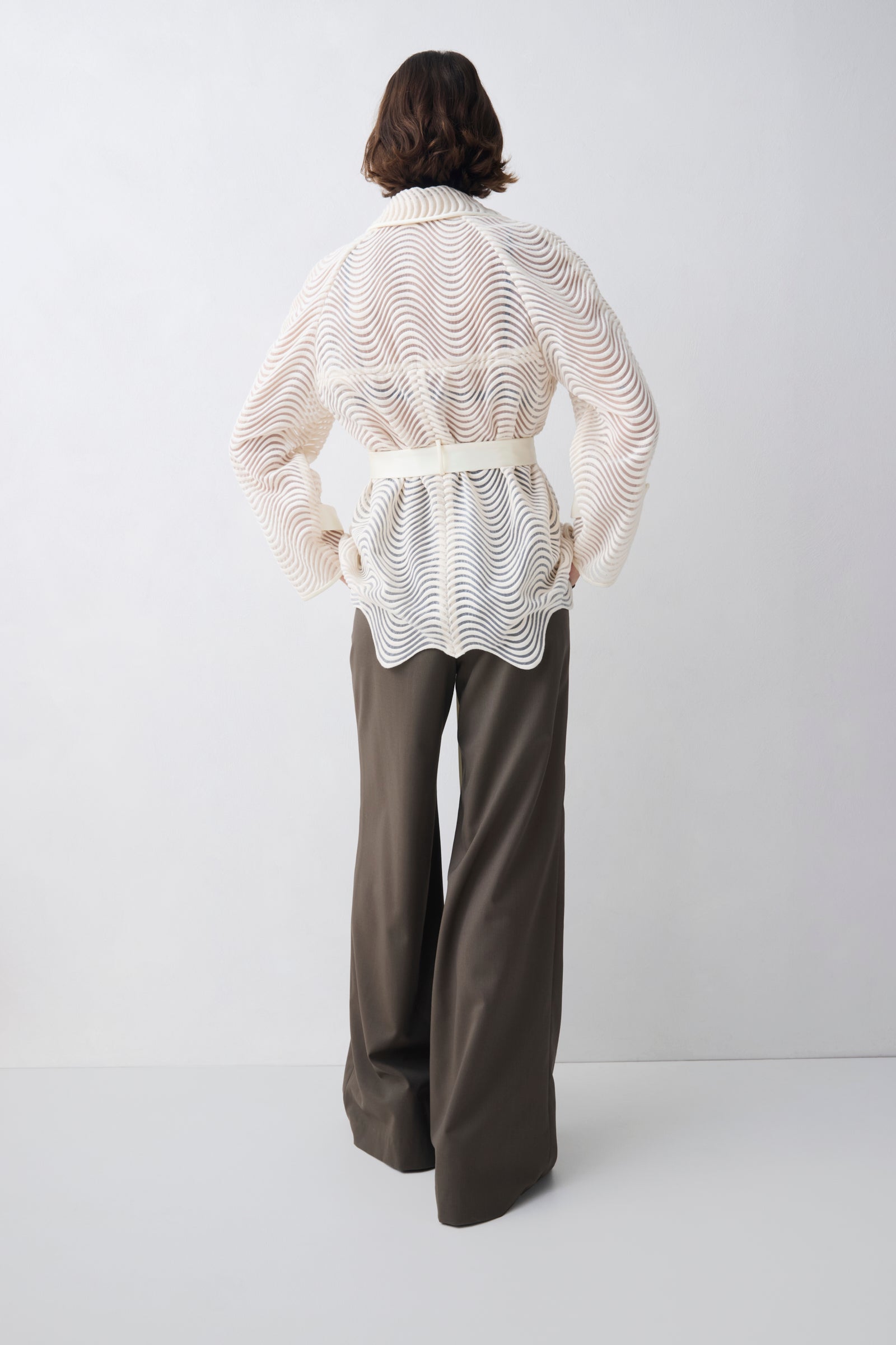 Person wearing a white patterned blouse and brown pants on a white background