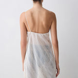 Woman wearing a white dress with a subtle pattern on a plain background