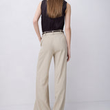 A woman is shown from behind wearing a black sleeveless top and beige wide-leg trousers with a thin black belt, standing against a light gray studio background.