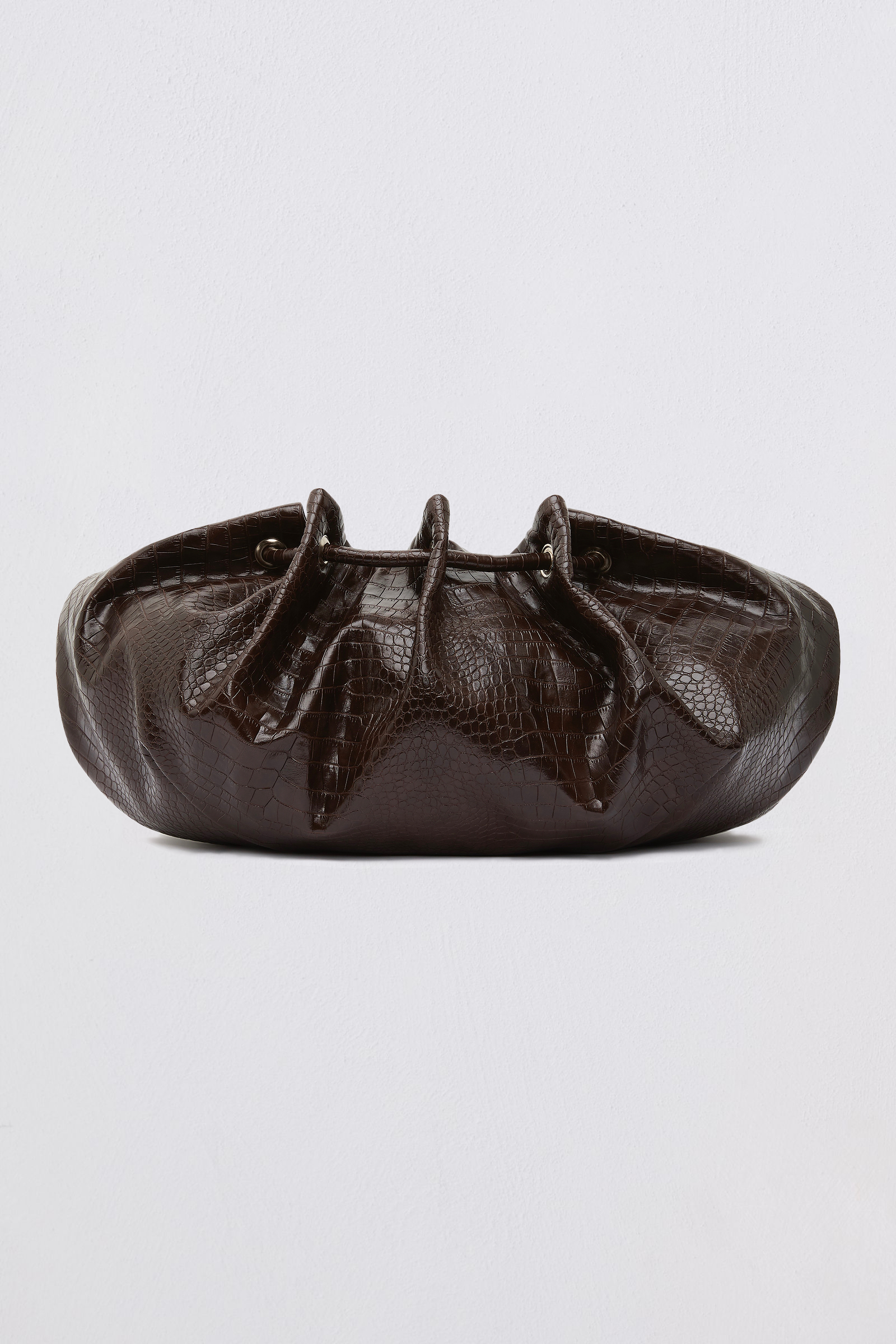 A dark brown textured leather clutch bag with a gathered, ruched top design, photographed against a neutral light gray background.