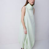 A woman modeling a sleeveless, high-neck, flowing maxi dress in a pale mint green color, standing against a plain light gray studio background.