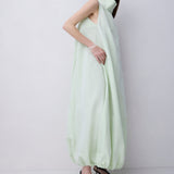 A model wearing a pale mint green sleeveless maxi dress with a high draped collar and voluminous gathered hem, paired with black strappy high-heeled sandals, against a plain light gray studio background.