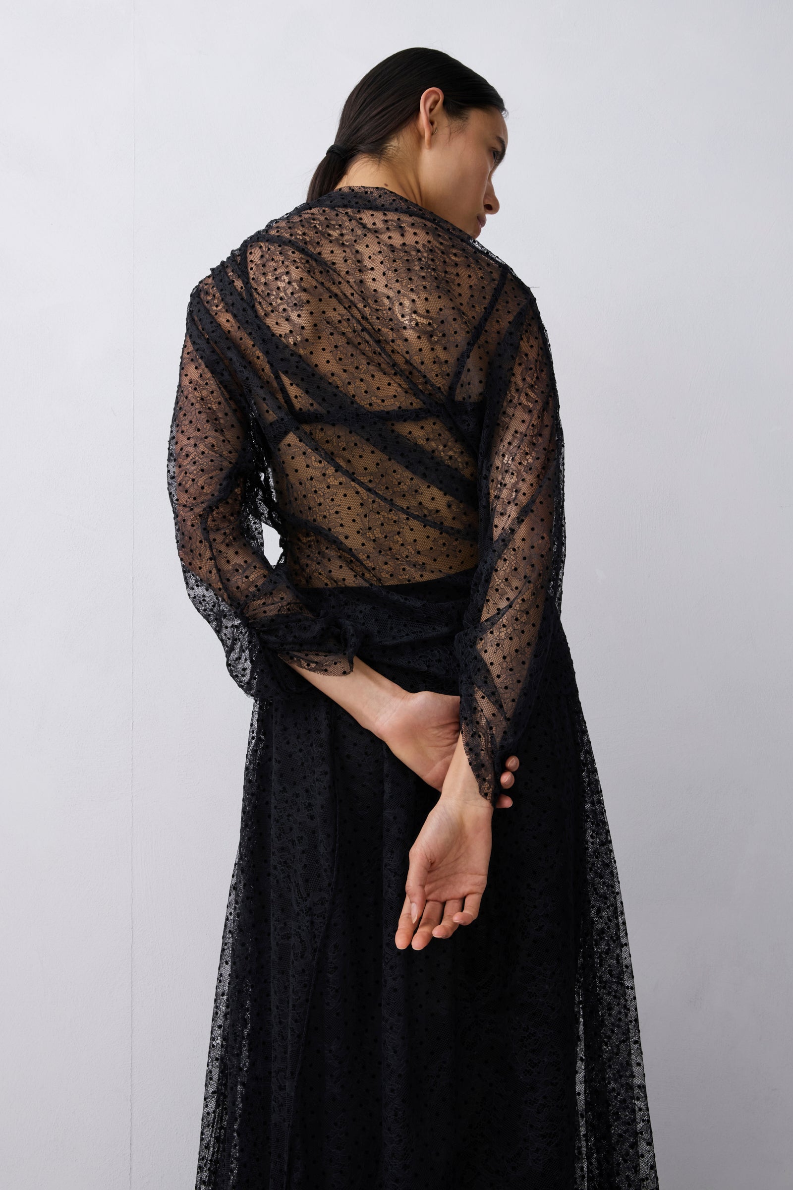 Woman wearing a black lace top against a plain background