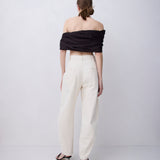 A model shown from the back wearing a black off-the-shoulder wrap top and cream wide-leg trousers with black strappy heels, set against a plain light gray studio background.