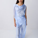 A model wearing a light blue draped two-piece outfit consisting of a sleeveless top and matching wide-leg pants, photographed against a seamless white studio background.