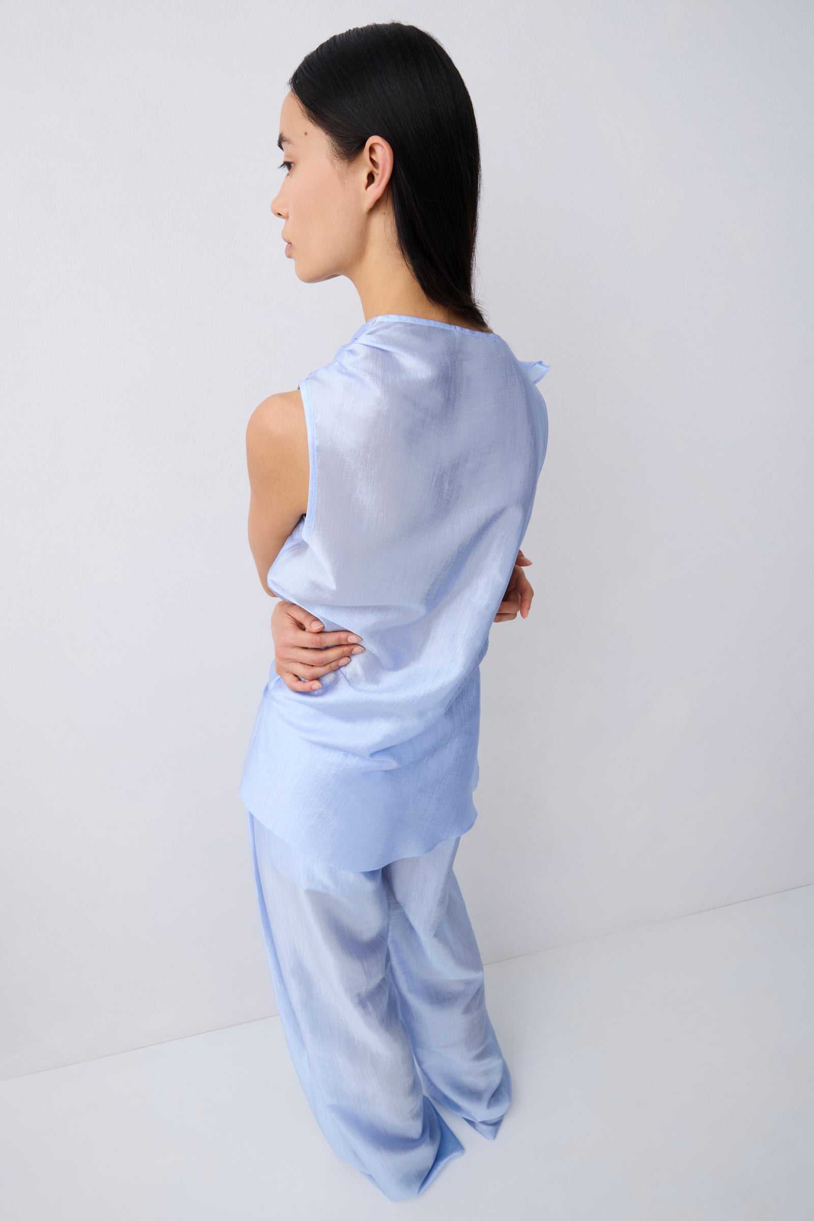 A woman wearing a light blue satin two-piece set, shown from the back in a studio setting with a white background.