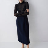 Woman wearing a black top and navy skirt against a white background