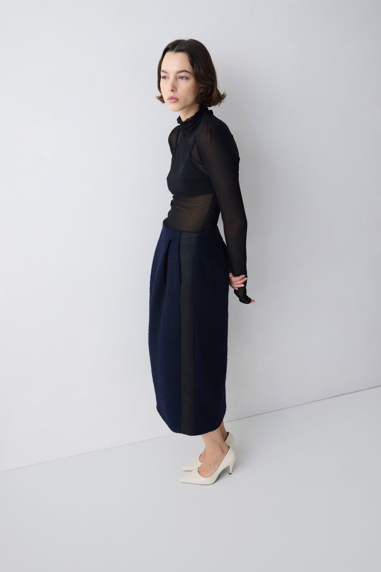 Woman wearing a black sheer top and navy skirt against a white background